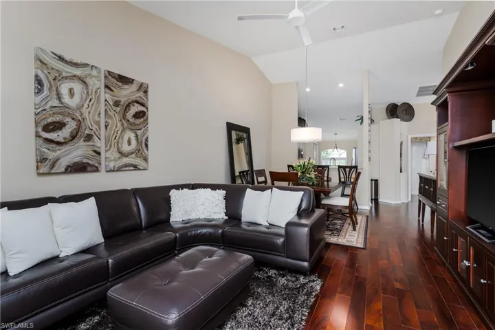 Vaulted ceiling living area featuring rich wood-finish flooring, a contemporary ceiling fan, and a built-in media console