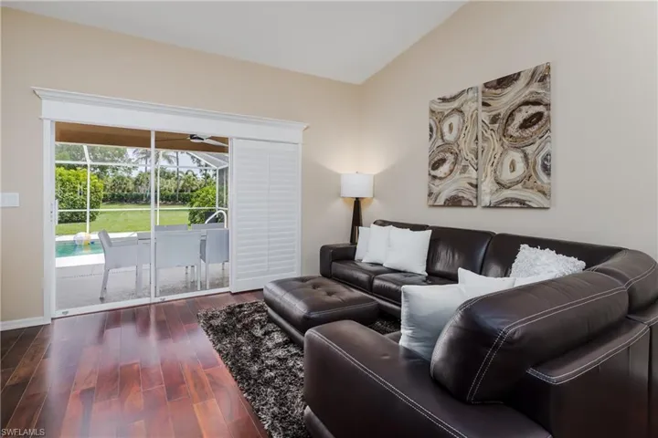 Living area featuring wood-finish flooring, vaulted ceilings, and direct access to the outdoor screened patio through sliding glass doors
