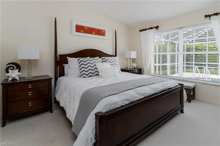 Vaulted ceiling room featuring a large window with white blinds, offering a view of an outdoor pool area with a white cage enclosure