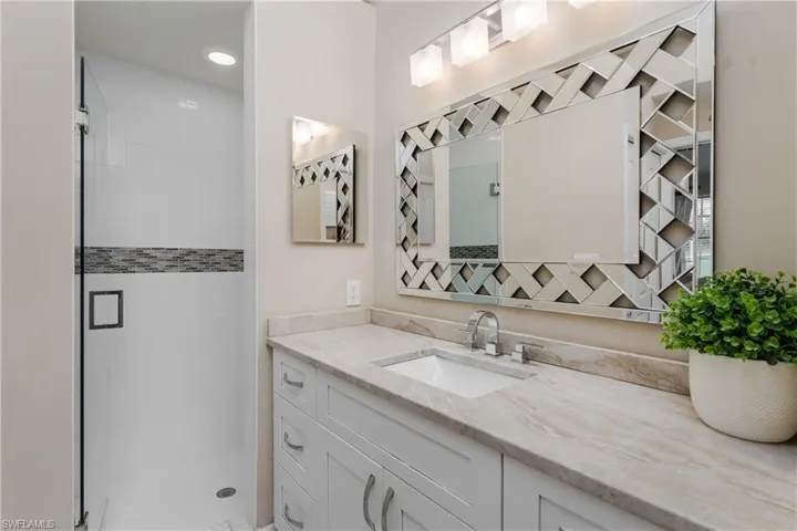 Spacious bathroom featuring a frameless glass shower enclosure with mosaic tile accent, a vanity with stone-finish countertop, undermount sink, and a decorative mirrored frame