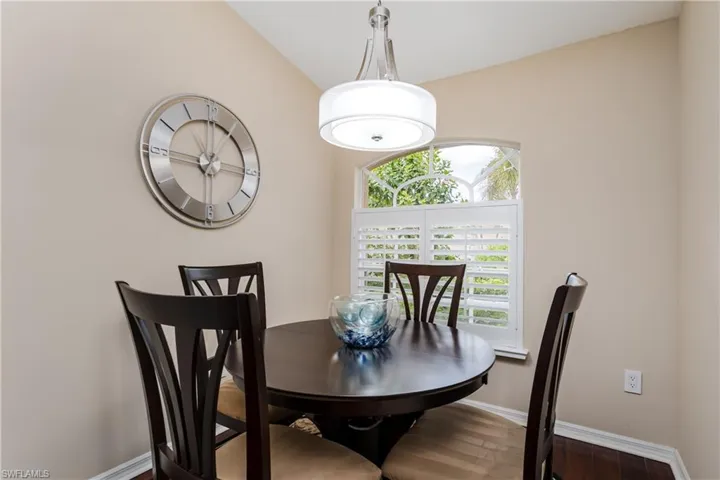 Vaulted ceiling above a dining area featuring hardwood flooring, an arched window with white plantation shutters, and a contemporary drum pendant light fixture