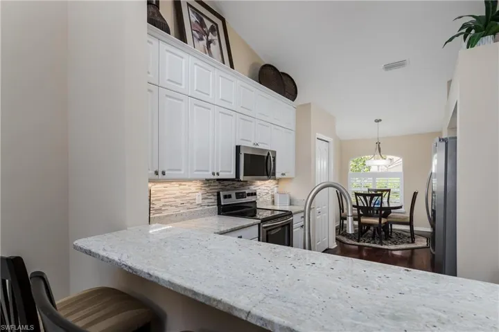Kitchen featuring a breakfast bar with stone countertop, white shaker cabinetry, stainless steel appliances, and a tiled backsplash
