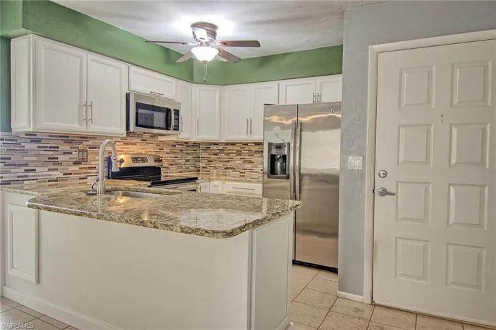 Kitchen featuring white cabinetry, a granite countertop island with an undermount sink, a mosaic tile backsplash, and stainless steel appliances including a refrigerator, microwave, and range