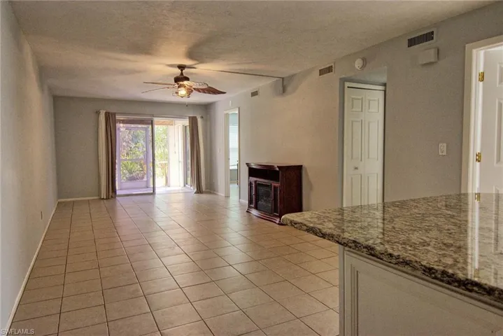Spacious open-concept room featuring tile flooring, a ceiling fan with integrated lighting, sliding glass doors to the exterior, and a built-in media console with an electric fireplace