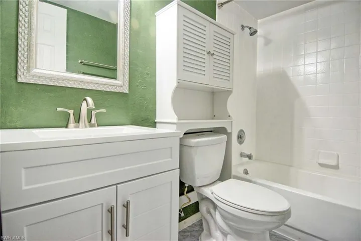 Full bathroom featuring a white vanity with integrated sink, brushed nickel faucet, decorative framed mirror, and a white tub with tiled shower surround