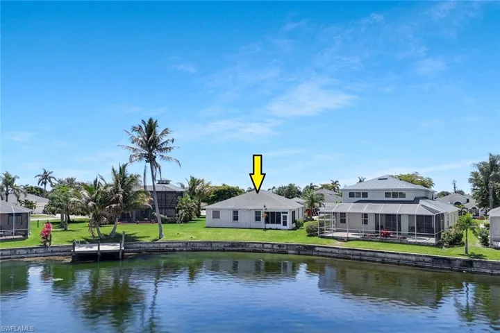 Waterfront property featuring a private dock, lush green lawn, mature palm trees, and a screened lanai