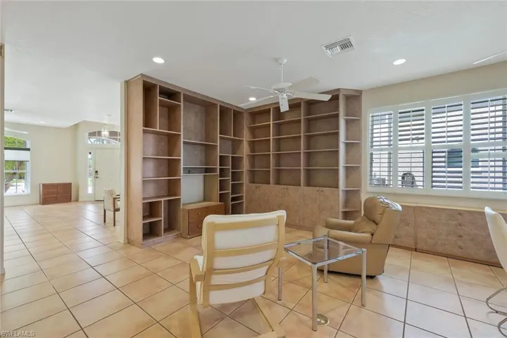 Family room features extensive built-in shelving, tile floors, plantation shutters, and ceiling fan