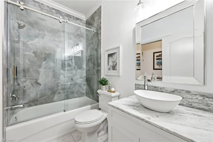 Renovated guest bathroom; tub to ceiling porcelain tile, glass shower sliding doors, marble top vanity with sink vessel and modern vanity lighting.
