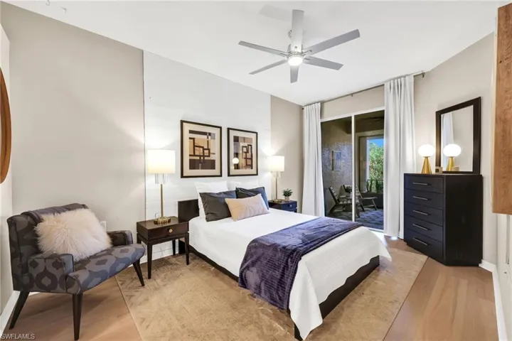 Primary bedroom with luxury flooring, paneled accent wall behind bed, modern ceiling fan/light, room darkening drapery panels.