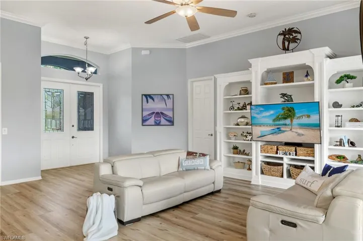 Living room with light wood-type flooring, ornamental molding, and ceiling fan with notable chandelier