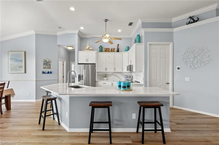 Kitchen with crown molding, a large island with sink, ceiling fan, tasteful backsplash, and light hardwood / wood-style flooring
