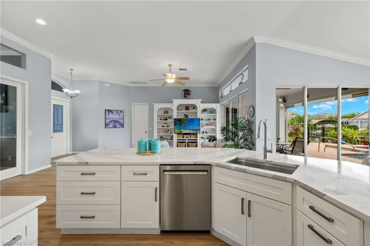 Kitchen featuring ceiling fan with notable chandelier, crown molding, dishwasher, white cabinetry, and sink