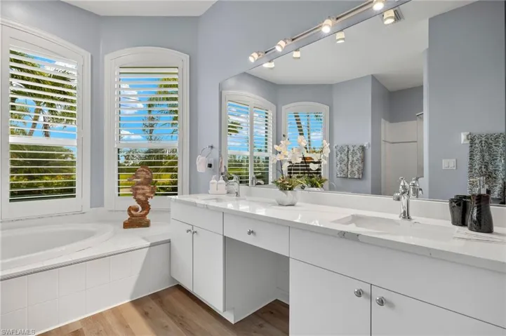Bathroom featuring tiled tub, dual bowl vanity, plenty of natural light, and hardwood / wood-style flooring