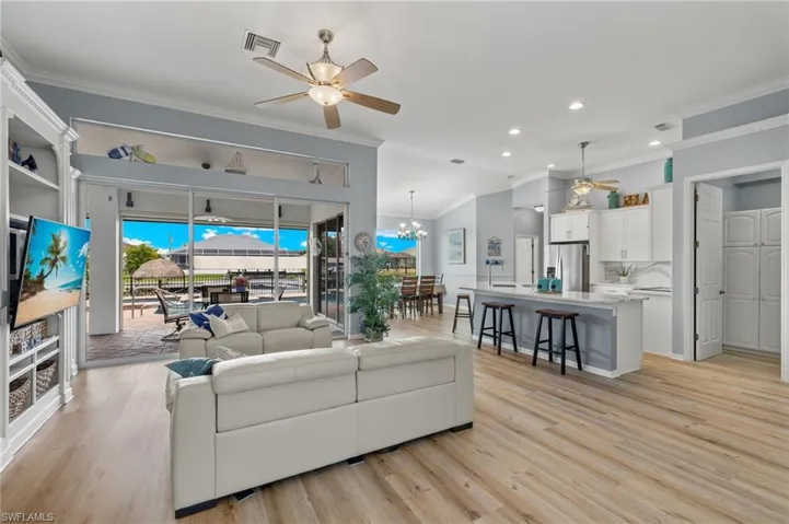 Living room featuring ceiling fan with notable chandelier, ornamental molding, and light hardwood / wood-style floors