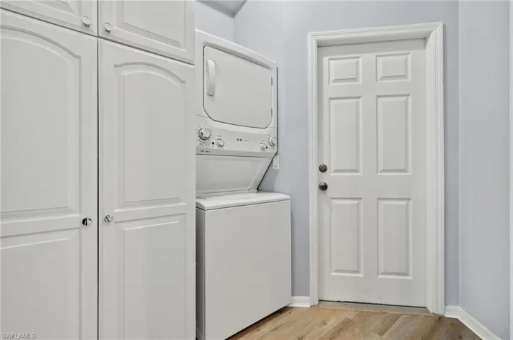 Washroom featuring stacked washer / dryer, cabinets, and light hardwood / wood-style floors
