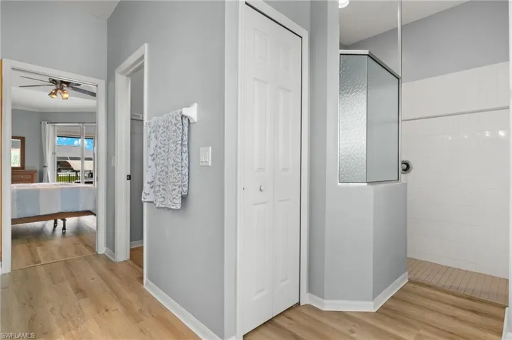 Bathroom with ceiling fan, a shower with door, and wood-type flooring