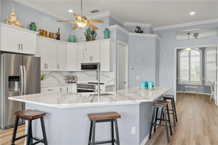 Kitchen with ceiling fan, white cabinets, light hardwood / wood-style floors, backsplash, and stainless steel appliances