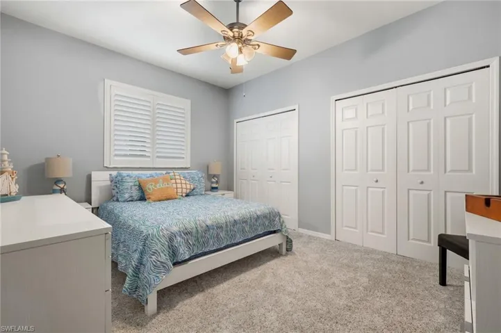 Bedroom with ceiling fan, two closets, and light colored carpet