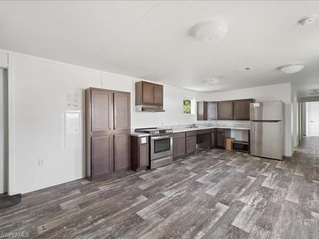 Kitchen with dark brown cabinetry, stainless steel appliances, light countertops, a sink, and dark wood-style floors