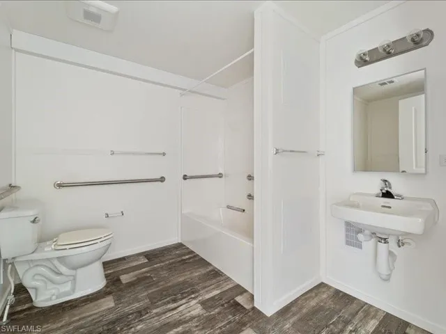 Full bath with wood finished floors, toilet, washtub / shower combination, and a sink