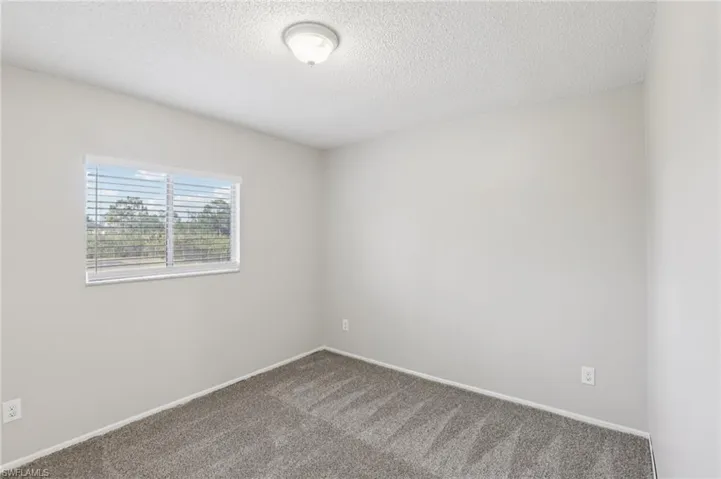 Carpeted empty room featuring a textured ceiling and baseboards