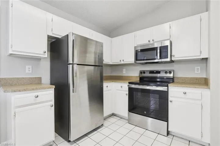 Kitchen featuring appliances with stainless steel finishes, vaulted ceiling, white cabinetry, light tile patterned flooring, and a textured ceiling