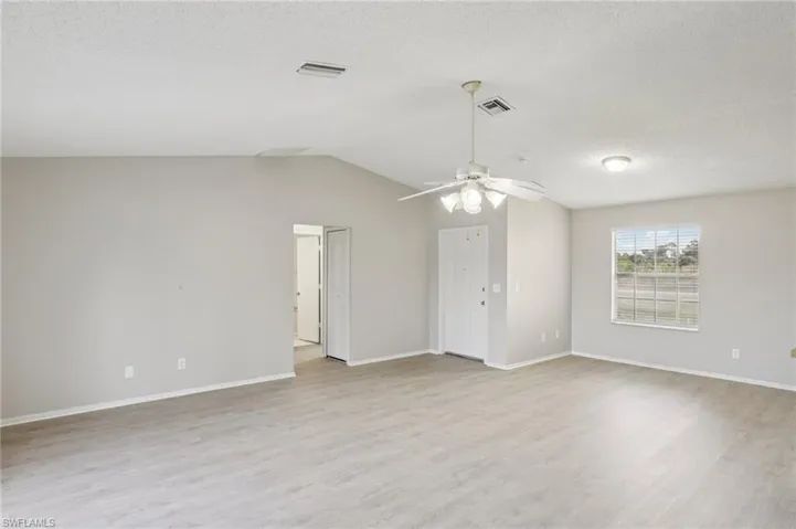 Unfurnished room featuring light wood-style flooring, a textured ceiling, and vaulted ceiling