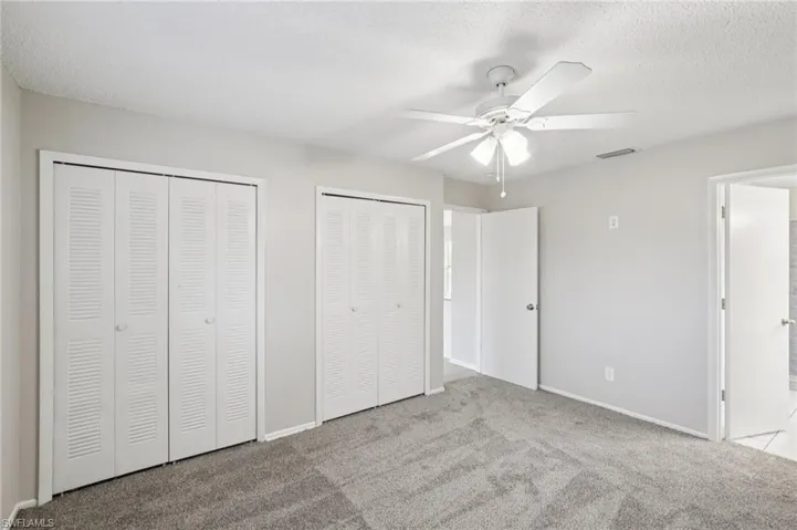 Unfurnished bedroom with two closets, light colored carpet, a textured ceiling, a ceiling fan, and connected bathroom
