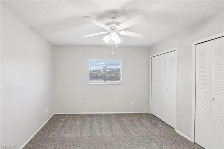Unfurnished bedroom with two closets, carpet floors, a textured ceiling, and ceiling fan