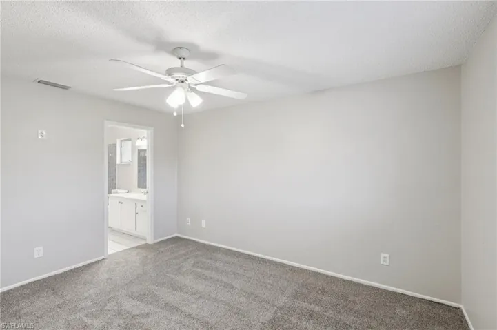 Empty room with light colored carpet, ceiling fan, and a textured ceiling