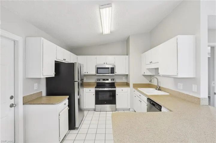 Kitchen featuring stainless steel appliances, lofted ceiling, a textured ceiling, white cabinets, and light tile patterned floors