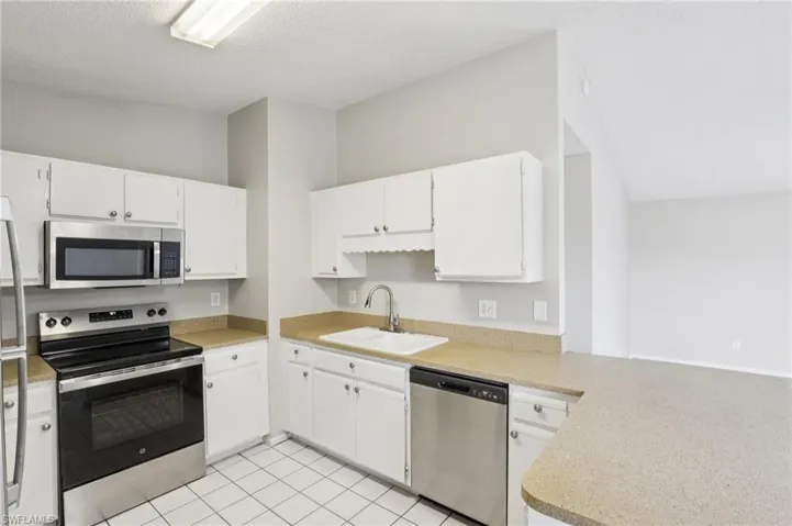 Kitchen with appliances with stainless steel finishes, a peninsula, white cabinets, light tile patterned floors, and light stone countertops