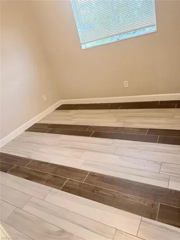 Ceramic tile flooring with alternating light and dark wood-look planks, neutral wall color, and white baseboards