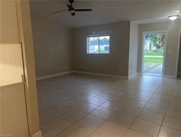 Spacious living area featuring neutral-toned walls, square tile flooring, and a modern ceiling fan