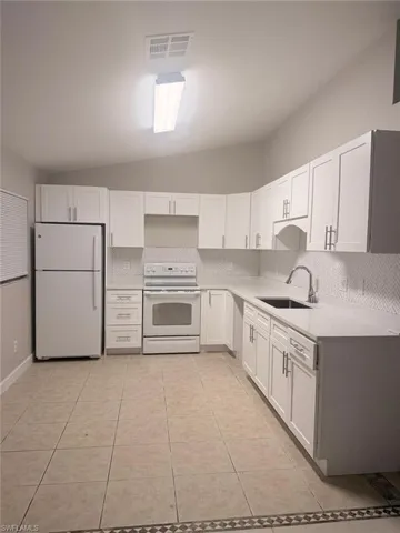 Contemporary kitchen featuring white cabinetry, light countertops, a herringbone tile backsplash, and ceramic tile flooring with a decorative border