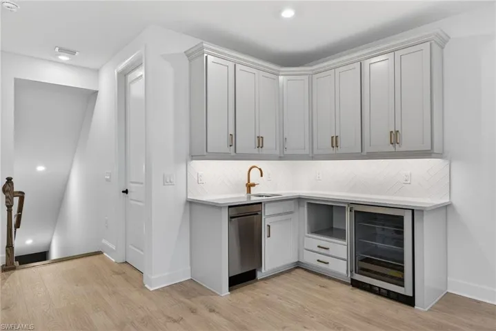 Bar area with beverage cooler, light stone counters, light wood finished floors, recessed lighting, and backsplash