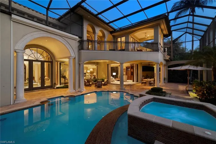 Back of house with a pool with hot tub, a patio area, a balcony, and a lanai