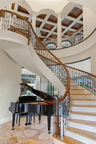 Staircase featuring beamed ceiling, tile patterned flooring, a high ceiling, ornate columns, and coffered ceiling