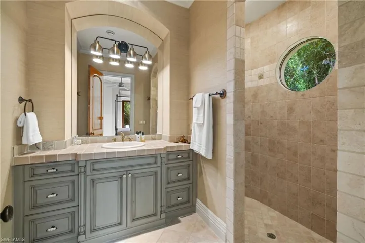 Bathroom featuring tiled shower, vanity, ceiling fan, and tile patterned floors