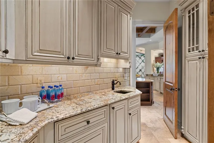 Kitchen with decorative backsplash, sink, light stone countertops, and light tile patterned floors