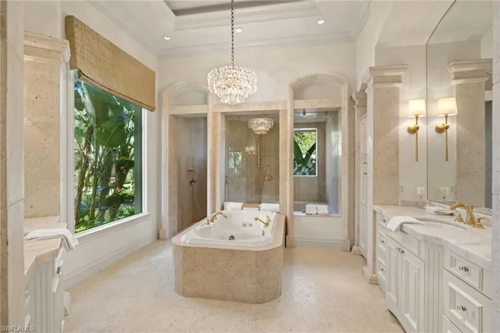 Bathroom with a notable chandelier, vanity, tiled tub, a raised ceiling, and tile patterned flooring