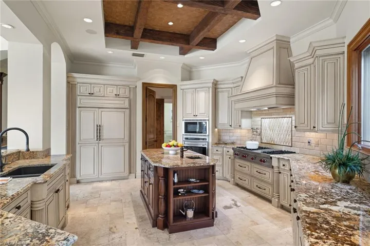 Kitchen with cream cabinets, sink, custom exhaust hood, and coffered ceiling