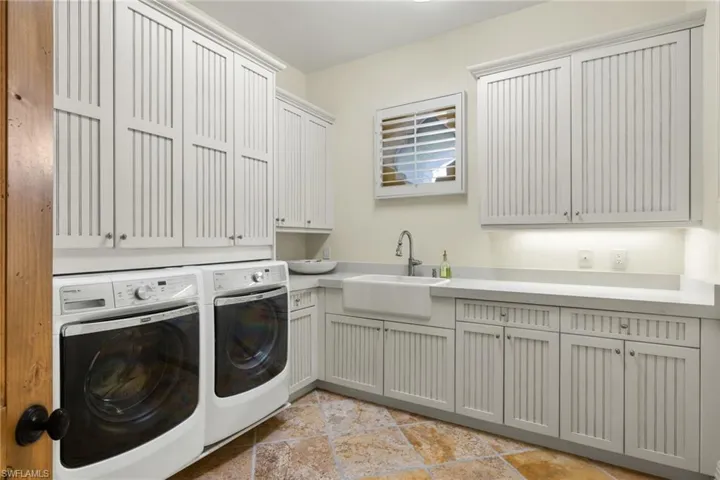 Laundry area with cabinets, light tile patterned floors, washing machine and dryer, and sink