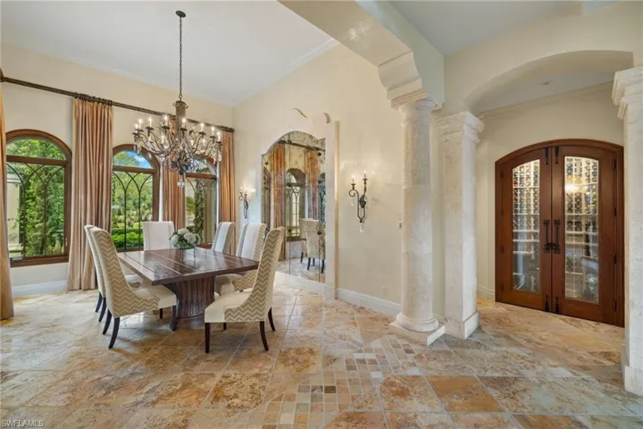 Dining area featuring an inviting chandelier, french doors, light tile patterned floors, crown molding, and ornate columns