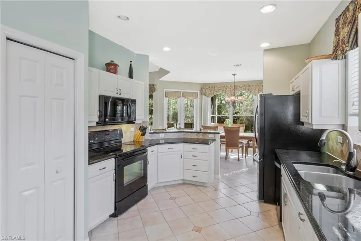 Kitchen featuring black appliances, white cabinets, a peninsula, light tile patterned floors, and suspended lighting