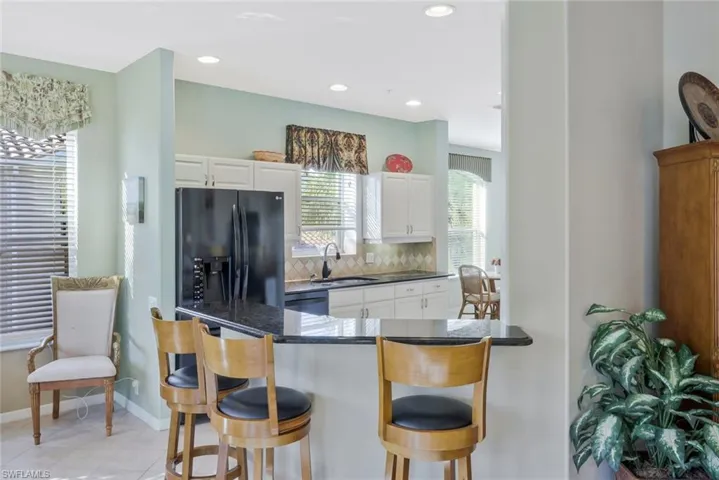 Kitchen with white cabinetry, a kitchen bar, black refrigerator with ice dispenser, backsplash, and recessed lighting