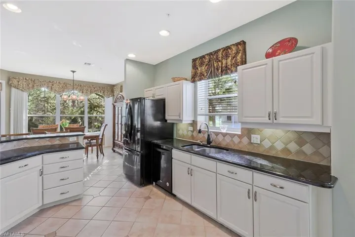 Kitchen with white cabinets, hanging light fixtures, black appliances, light tile patterned flooring, and dark stone countertops