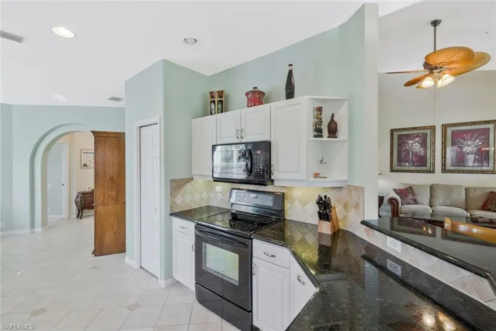 Kitchen featuring black appliances, dark stone counters, arched walkways, white cabinetry, and ceiling fan