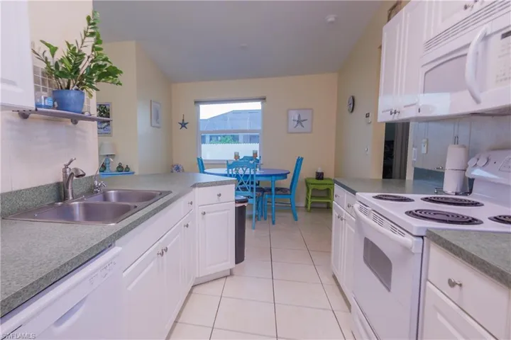 Kitchen with white appliances, white cabinets, light tile patterned flooring, and a peninsula