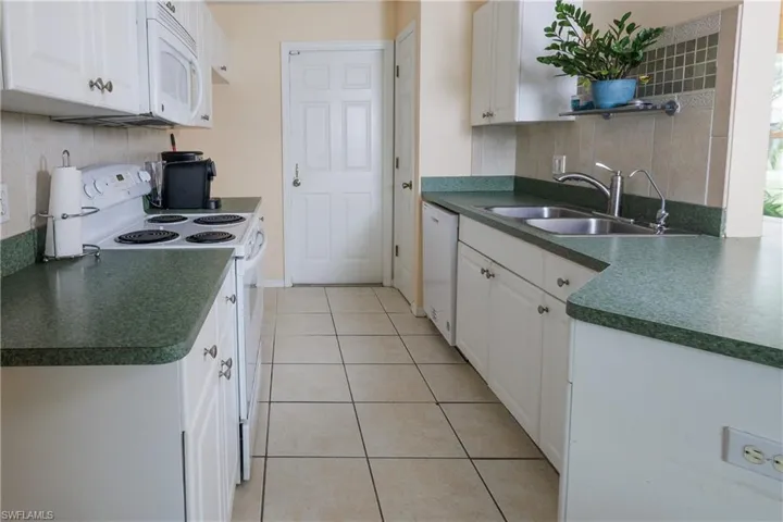 Kitchen with white appliances, dark countertops, light tile patterned floors, and white cabinetry
